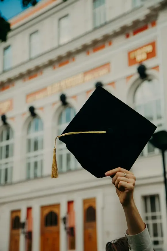 Graduate holding a cap against a bright sky